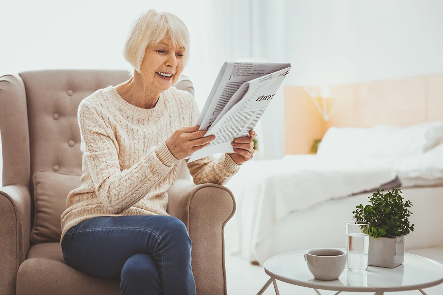 Aeltere Frau sitzt nachdenklich mit Buch im Wohnzimmer - Symbolbild fuer unsichtbare Beschwerden bei Polyneuropathie